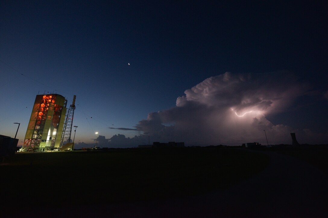 A lightning strike brightens a cloudy sky at a launching pad.