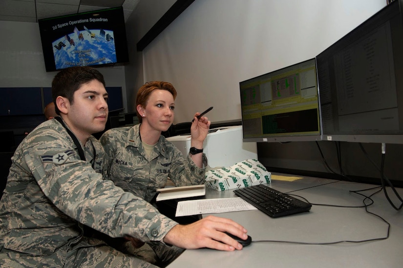 Two airmen work at a computer.