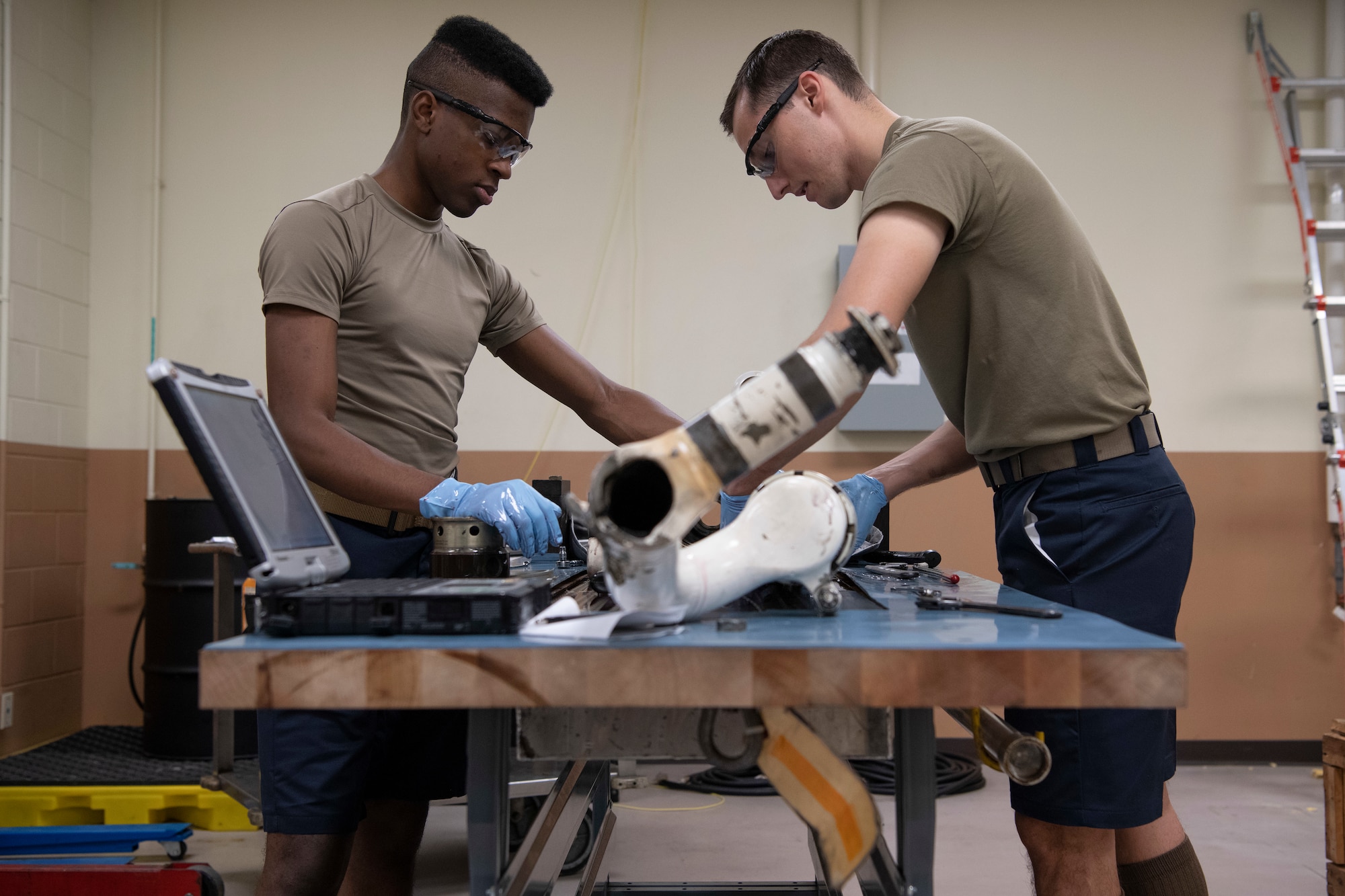 U.S. Air Force Airman 1st Class Christopher Swint, and Senior Airman Bryan Poole, 18th Component Maintenance Squadron hydraulics specialists, perform maintenance on an F-15C Eagle landing gear Jan. 14, 2020, at Kadena Air Base, Japan.  Airmen from the 18th Maintenance Group who work on the flight line are now authorized to wear shorts to help alleviate some of the heat stress brought on by the Okinawa climate. (U.S. Air Force photo by Senior Airman Rhett Isbell)