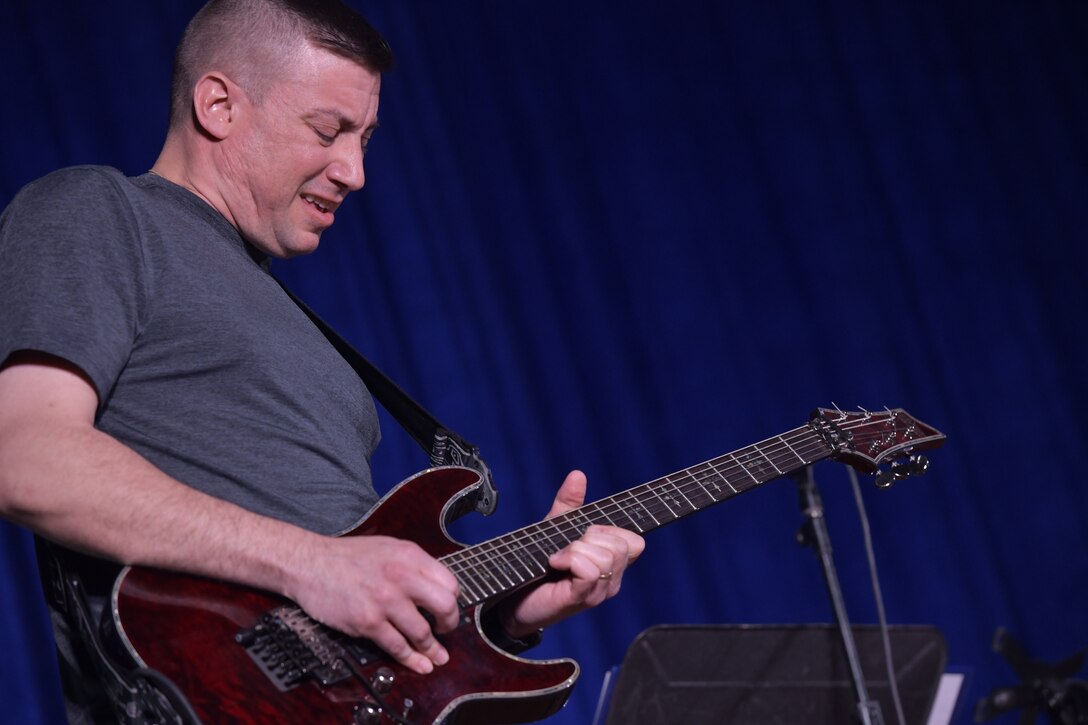 Tech. Sgt. Andrew Minns, Air Forces Central Command Band member, plays a guitar solo during his performance for deployed members in The Rock theater at Ali Al Salem Air Base, Kuwait January 3, 2020. The AFCENT Band is comprised of Airmen that have been selected by musical proficiency and then travel communicating to deployed members and local communities through music. (U.S. Air Force photo by Tech. Sgt. Alexandre Montes)