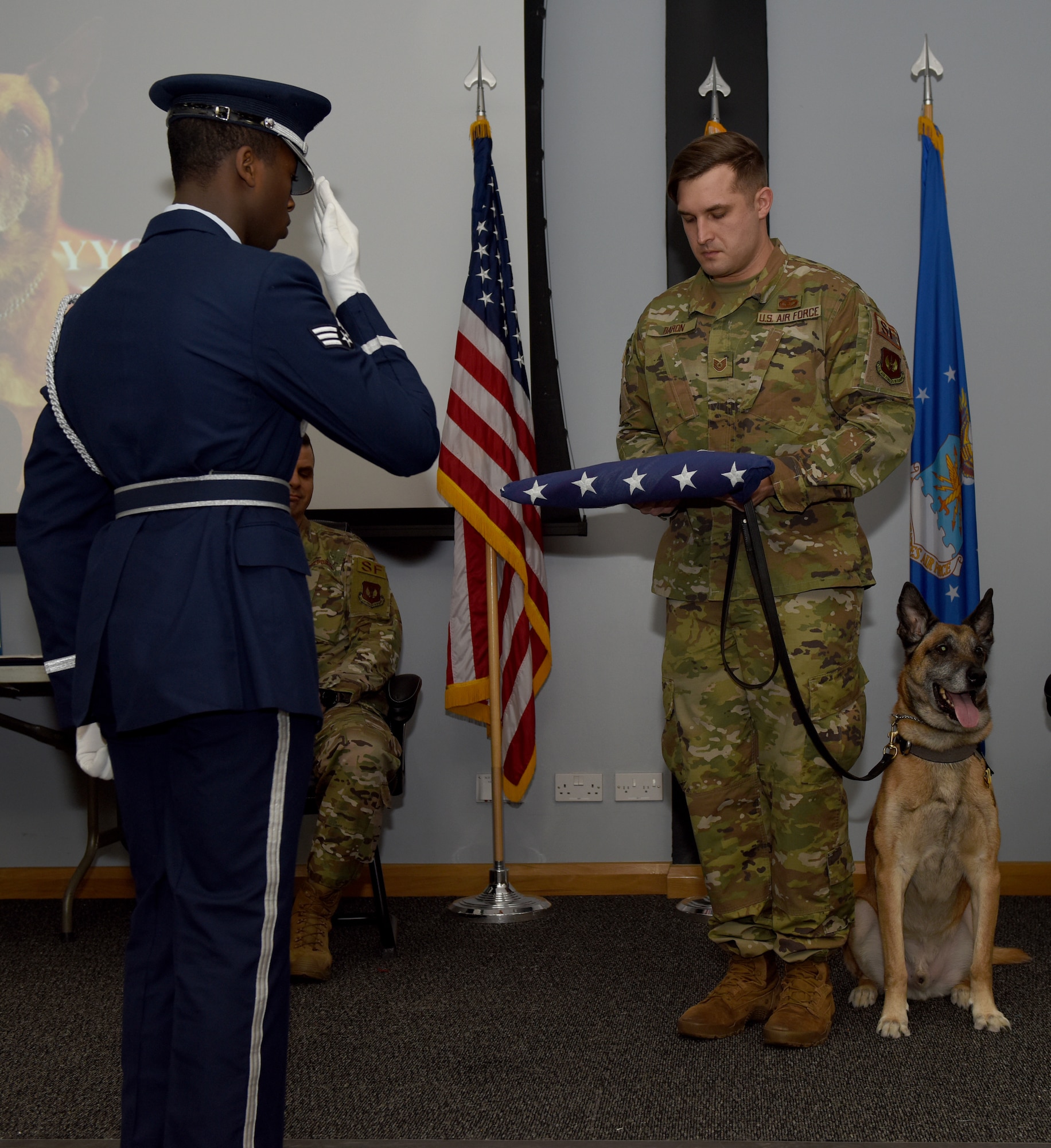 Tech. Sgt. Alexander Baron, a 48th Security Forces Squadron military working dog handler, accepts an American flag from an Honor Guardsman during a retirement ceremony for YYogi, a 48th SFS MWD, at Royal Air Force Lakenheath, England, Jan. 30, 2020. During his 10 years of service, he was a part of the first joint training with the 57th Rescue Squadron where he provided patrol and explosive detection dog security for the pararescuemen as they carried out their objectives from CV-22 Ospreys. (U.S Air Force photo by Airman 1st Class Jessi Monte)