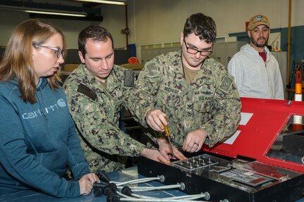 NNSY Electrician Amanda Herron (Code 950) teaches ET2 (SW) Bonner Secrest (SurgeMain Norfolk) and EM2 Tyler Smith (SurgeMain Columbus) how to fix electric panels.