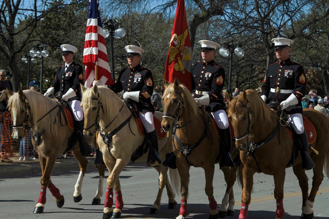 Marines ride horses in the street during a parade.