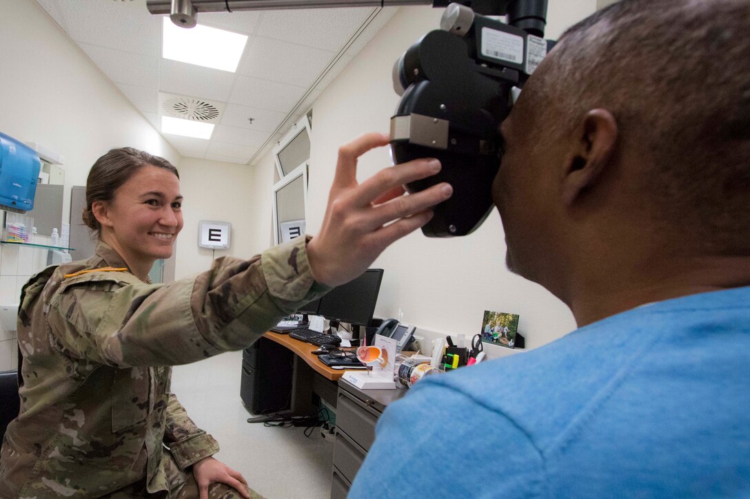 A soldier uses a phoropter to look at a patient's eyes.