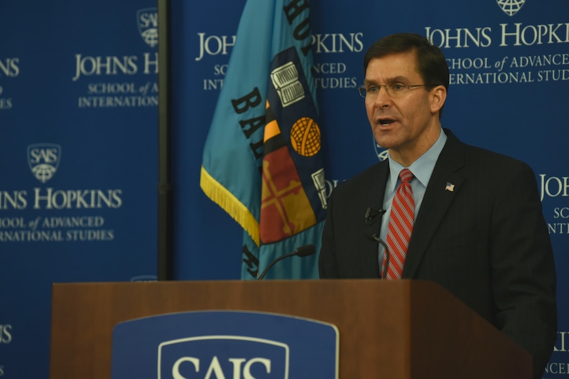 A man stands in front of an audience and talks into a microphone.