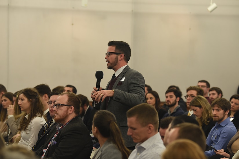 Audience member stands and holds a microphone while asking a question.