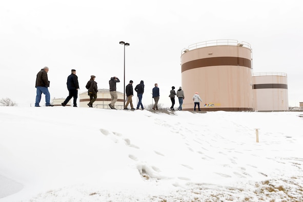Nine people walking outside in a line toward large fueling tanks.