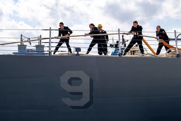 Sailors pull a rope on the deck of a ship.