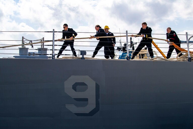 Sailors pull a rope on the deck of a ship.