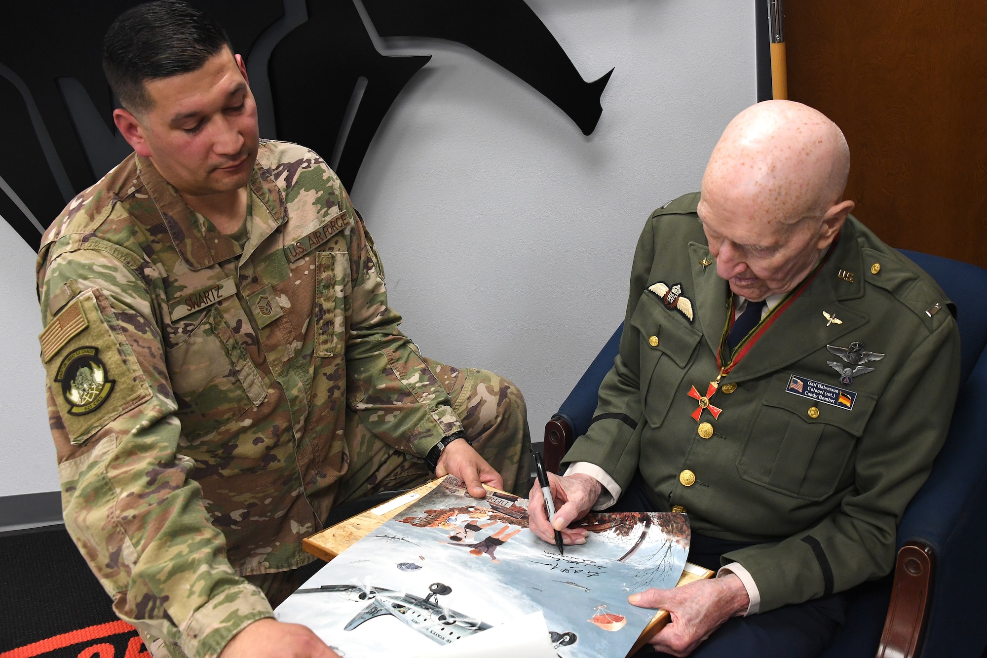 U.S. Air Force retired Col. Gail S. Halvorsen,  right, the Berlin Candy Bomber, autographs a photo for Master Sgt. Christopher Swartz, left, 821st Contingency Response Squadron aerial port flight chief, Jan. 31, 2020, Travis Air Force Base, California. As part of his visit, Halvorsen visited the 821st CRS where he spoke about the importance of being a part of the airlift team and told Airmen there was no greater service than to save the lives of others. (U.S. Air Force photo/ TSgt Liliana Moreno)