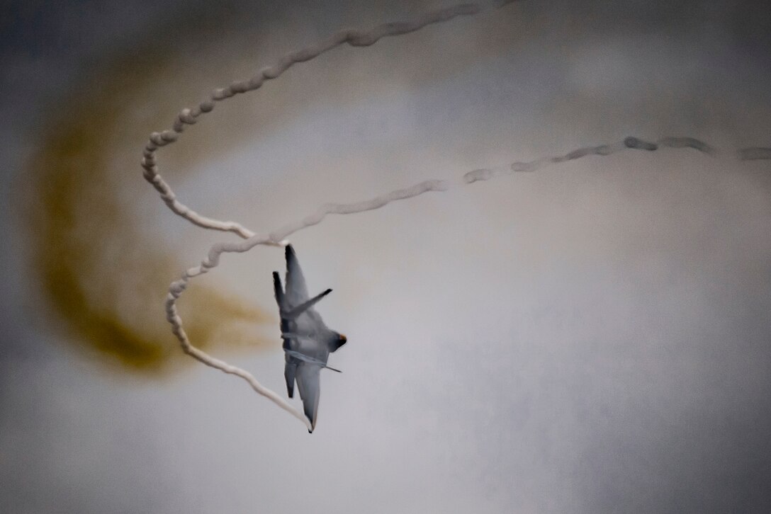 An aircraft flies in cloudy skies creating smoke trails from its wings.