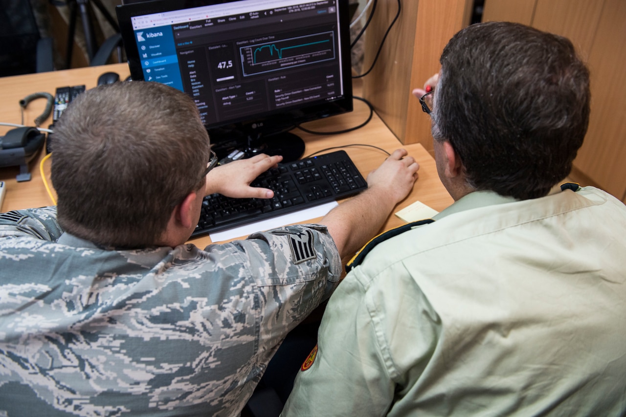 A U.S. airman and a service member from Montenegro work together at a computer monitor.