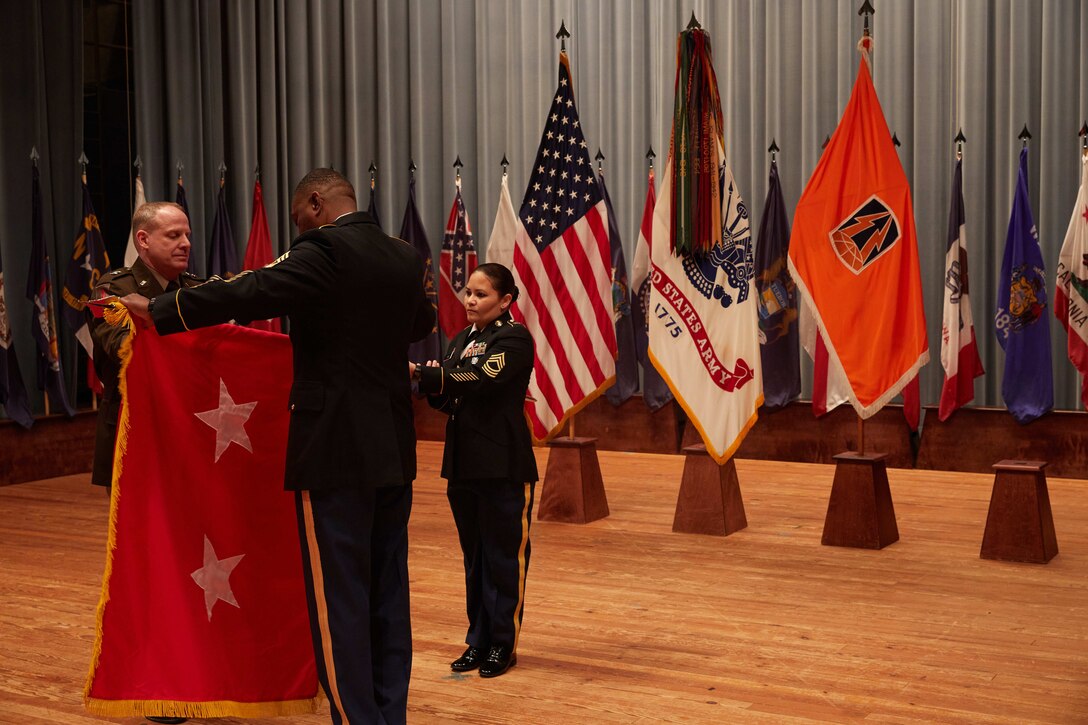 U.S. Army Reserve Maj. Gen. John Phillips (left) and Command Sgt. Maj. Edward Simpson unfurl his 2-star flag during his promotion ceremony held in Alexander Hall, Fort Gordon, Ga. Feb. 9, 2020.