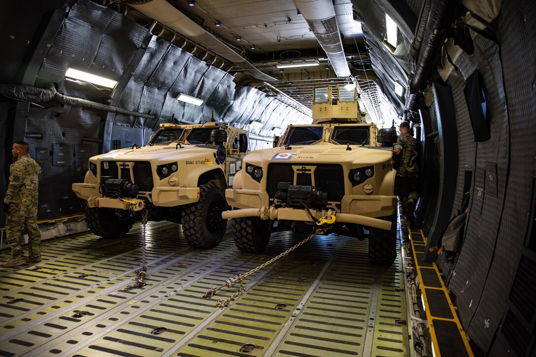 Two wheeled vehicles set side-by-side inside the hold of a military aircraft.