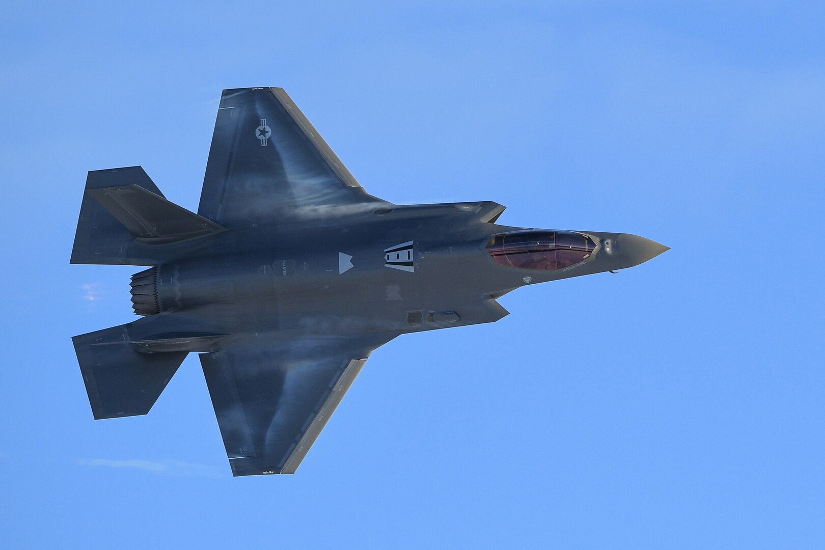 A military fighter aircraft makes a turn against a blue sky.