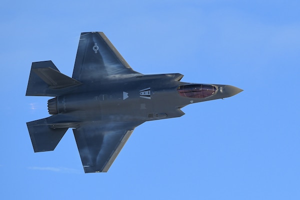 A military fighter aircraft makes a turn against a blue sky.
