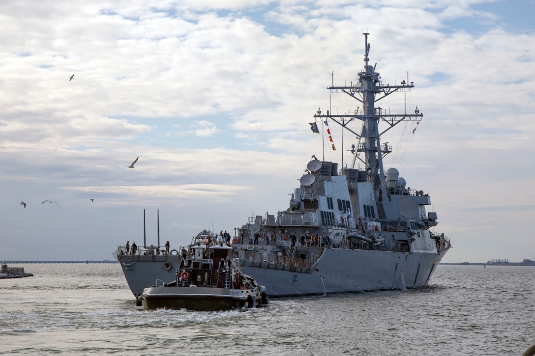 A large military ship is pulled through the water by a smaller ship.