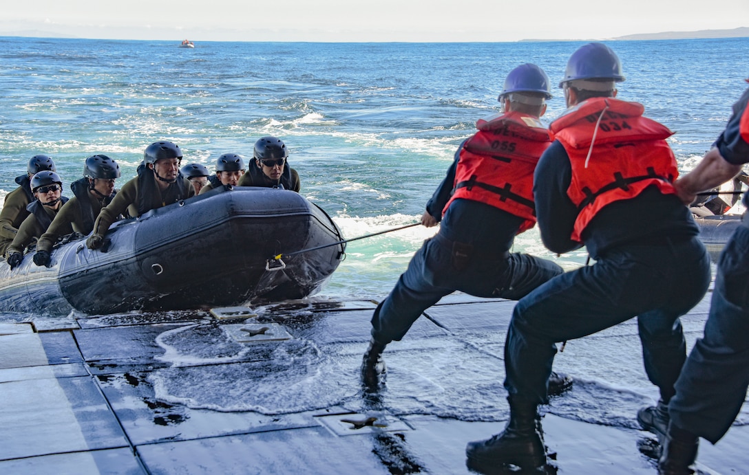 U.S. sailors pull a rope attached to a small boat carrying Japanese soldiers.