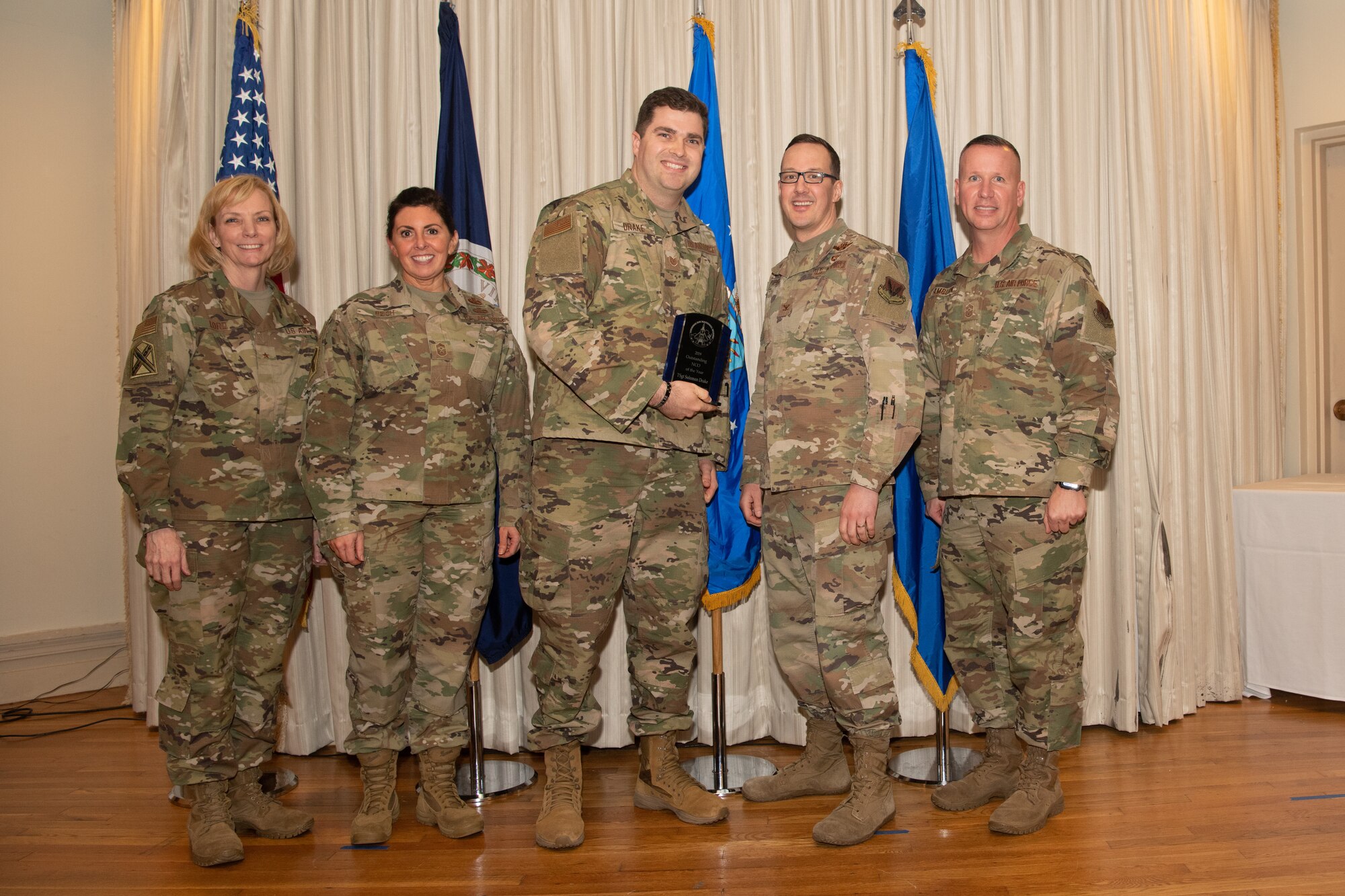 Airmen on a stage pose for a photo with award