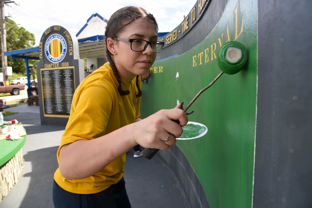 A sailor uses a paint roller to paint on a wall.