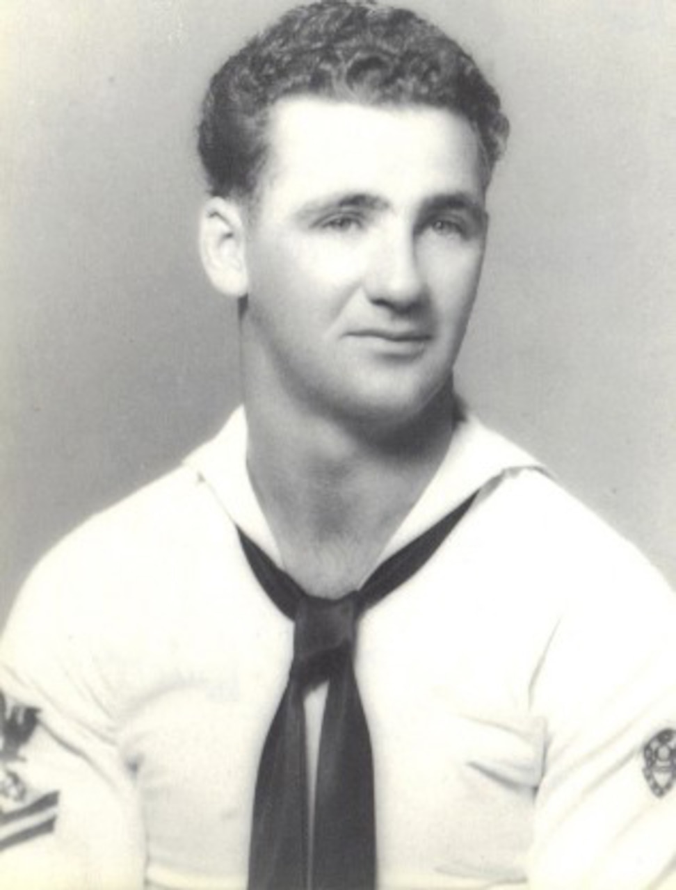 A sailor wearing a white dress uniform poses for the camera.