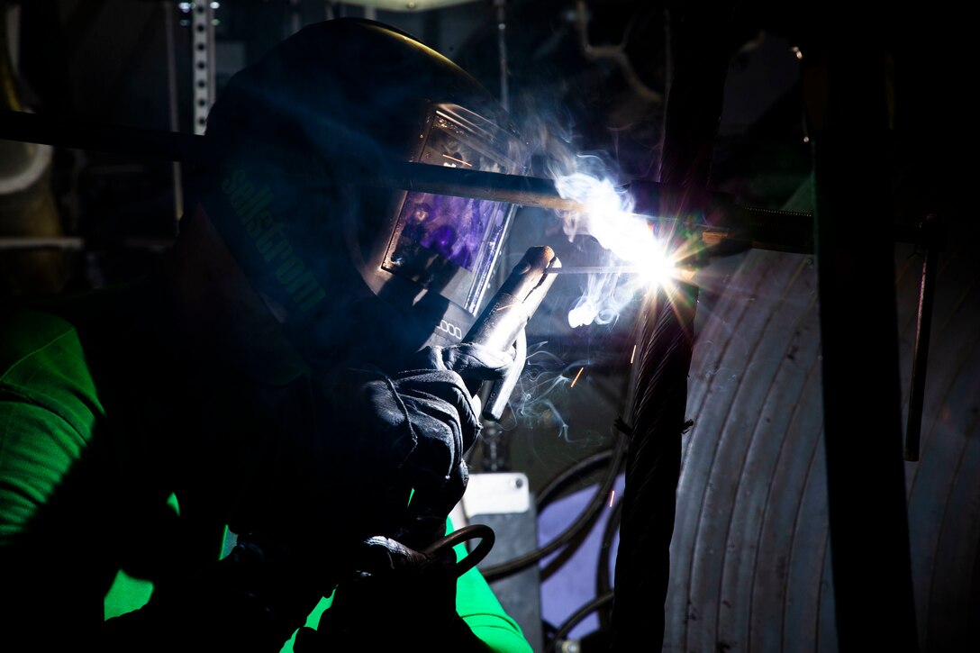 A sailor wearing protective gear welds wires.