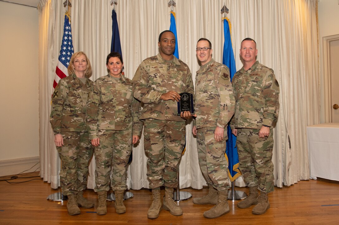 Airmen on a stage pose for a photo with award