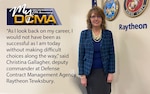 A smiling woman wearing a blue blazer and black skirt stands against a wall by military service logos.