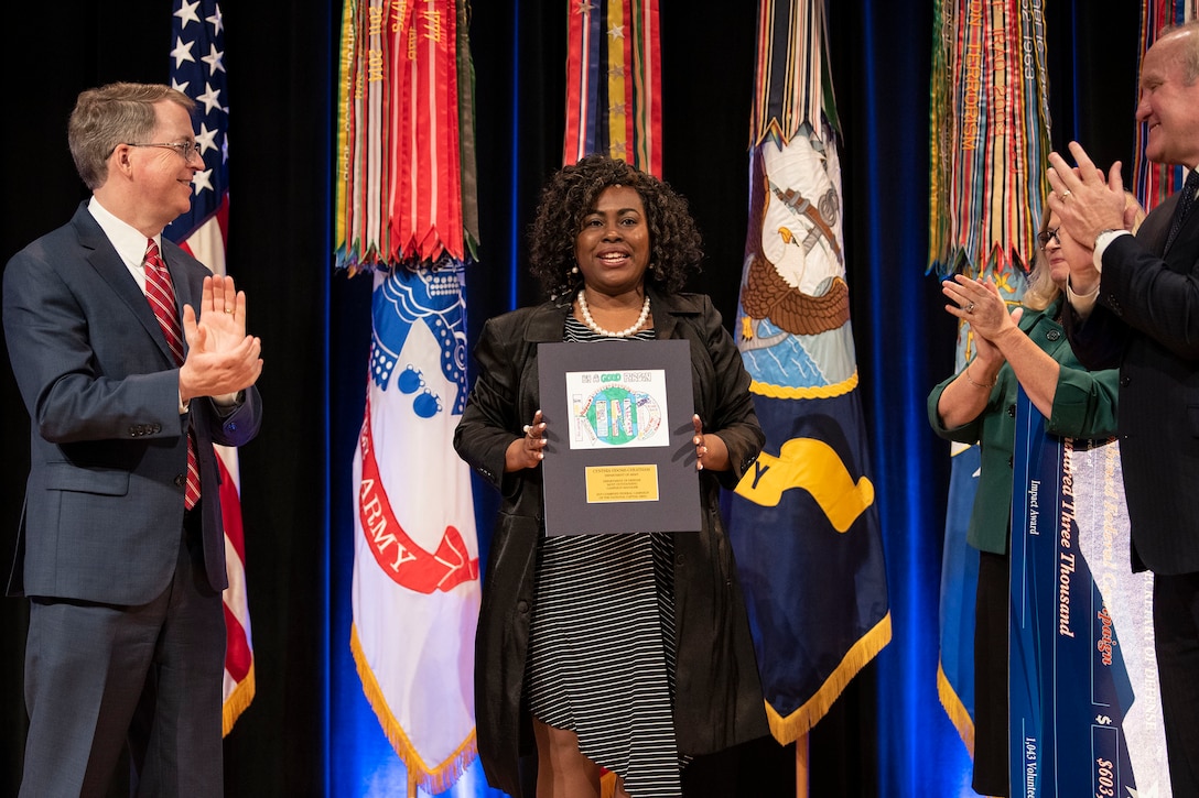 A woman stands in the center holding up a plaque; people stand on either side.