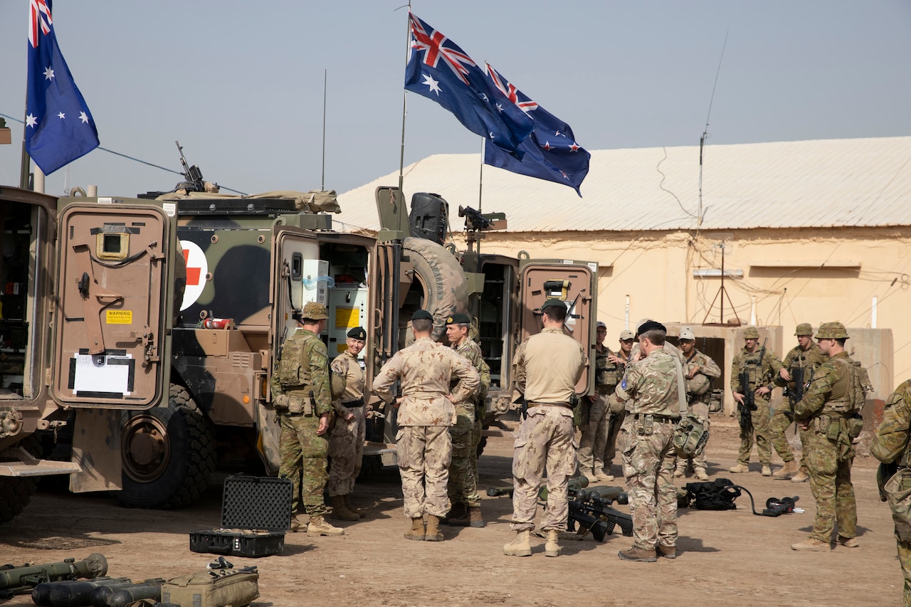 Service members stand near military vehicles.