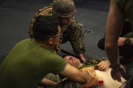 Marines with the 31st Marine Expeditionary Unit (MEU) and Sailors with the amphibious assault ship USS America (LHA 6) assess a simulated casualty after transport via stretcher during a Tactical Combat Casualty Care (TCCC) exercise.