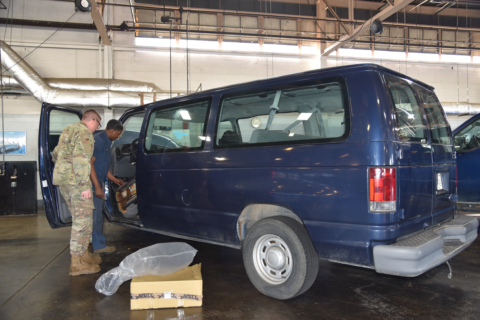 A man in blue coveralls fixes a mini van