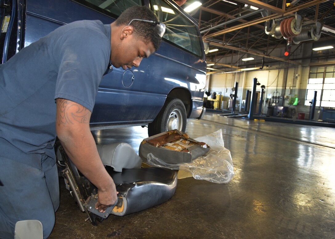A man in blue coveralls fixes a mini van