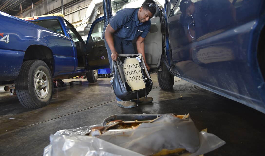 A man in blue coveralls fixes a mini van