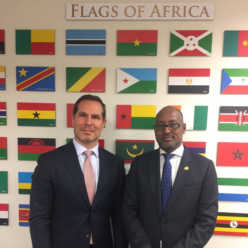 Two men stand in front of a wall with small flags affixed to it.