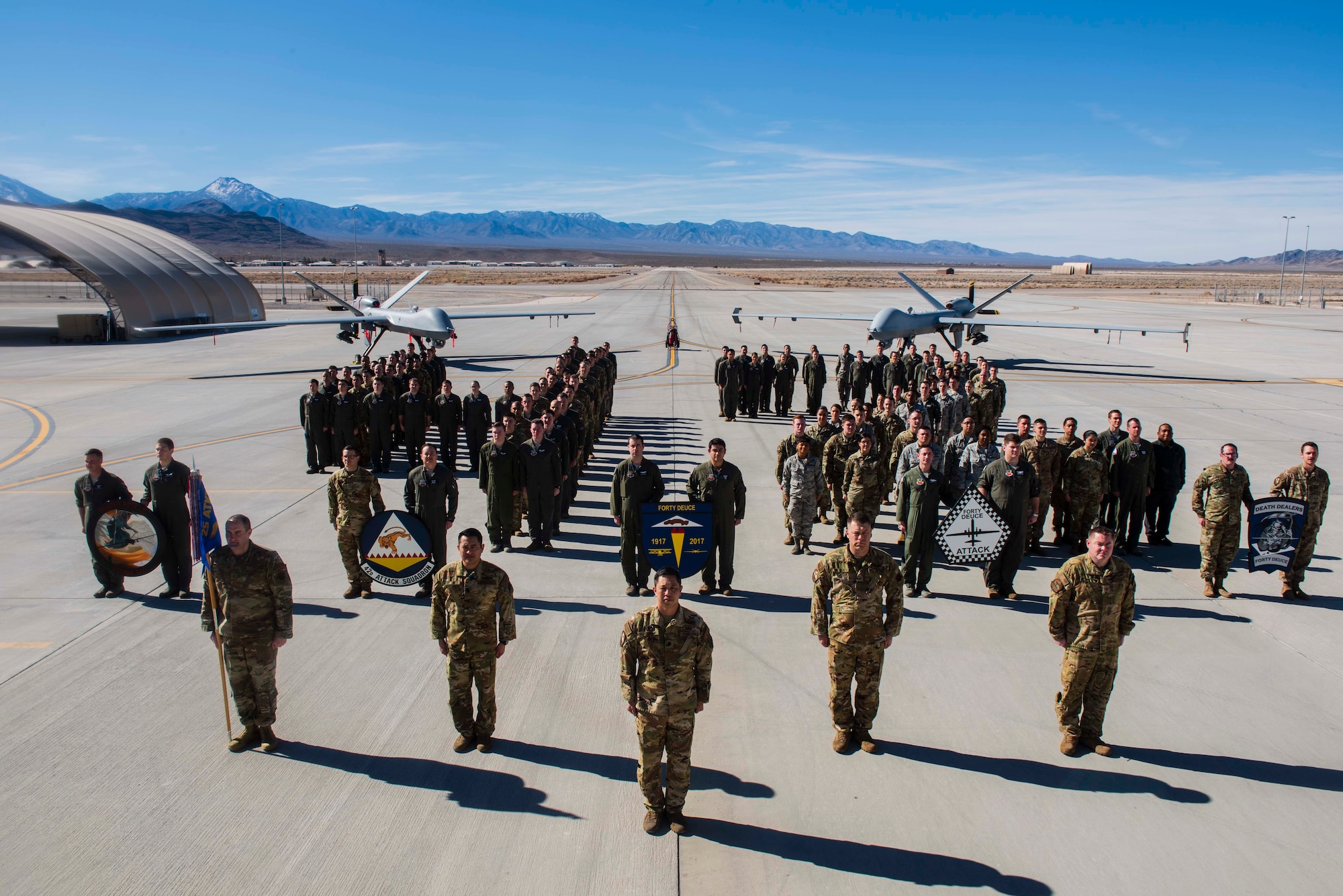 The Airmen of the 42nd Attack Squadron forms a "42" on the flightline in front of two MQ-9 Reapers.