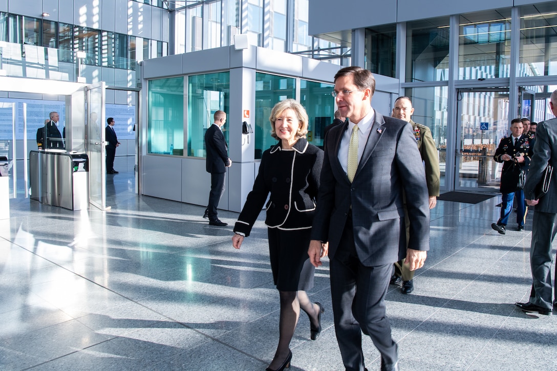 A man and a woman walk through a large glass building.