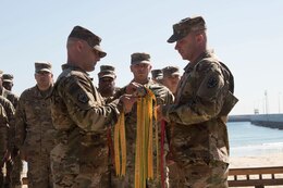 Chief Warrant Officer 4 Nicholas Laferte, commander, and Sgt. 1st Class Benjamin McGalliard, first sergeant, 492nd Theater Harbormaster Operations Detachment (THOD), hang campaign streamers on their unit colors to recognize past achievements and events of the 492nd THOD during their end of mission ceremony at Kuwait Naval Base, Feb. 13, 2020.