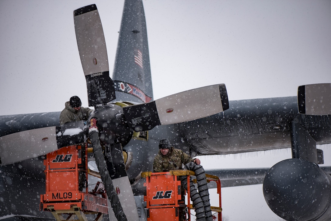 Airmen work on an aircraft as it snows.