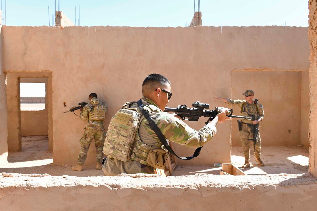 Three airmen hold weapons in an unfinished building.