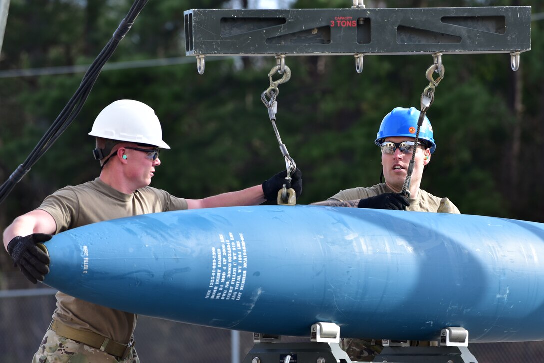 A1C Brandon Hunt, left, 4th Munitions Squadron stockpile surveillance technician, and Senior Airman Cameron Kosmerick, right, 4th MUNS conventional maintenance crew chief, set a bomb body onto a munitions assembly conveyer.