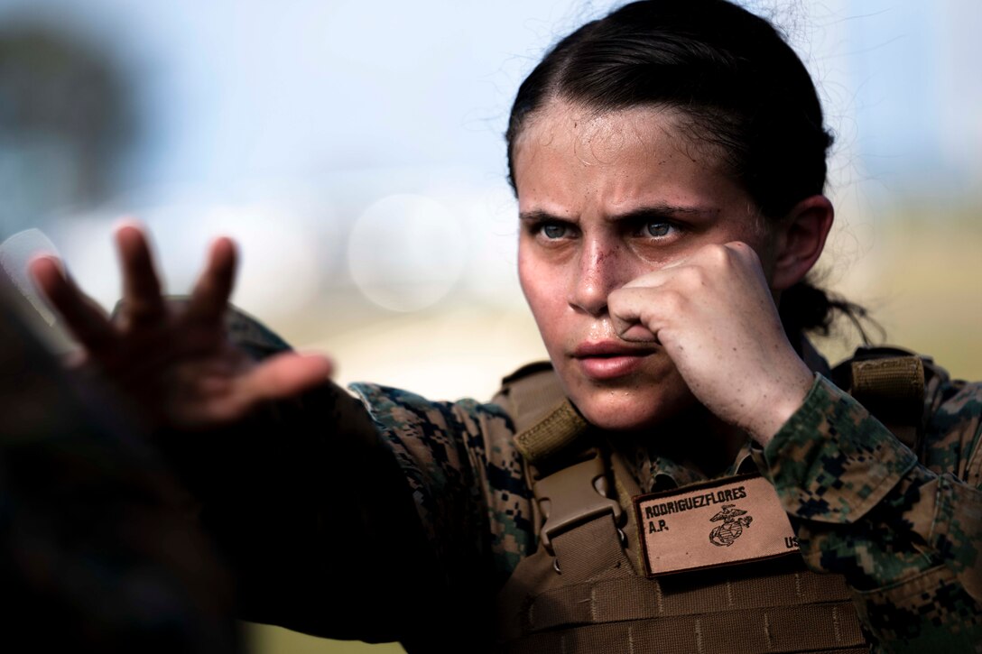 A Marine throws one hand forward while holding the other hand close to her face in a fist.