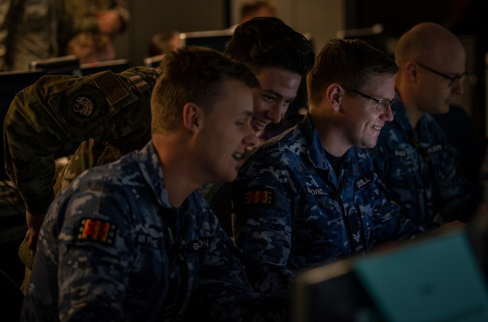 A U.S Air Force Airman and Royal Australian Air Force members look at a computer screen.