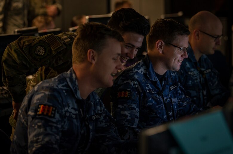 A U.S Air Force Airman and Royal Australian Air Force members look at a computer screen.