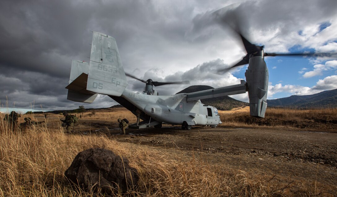 A Marine aircraft sits in an open field as service members exit.