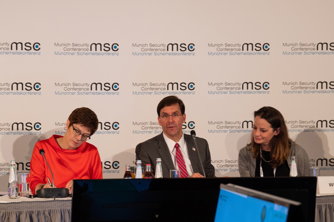 Defense Secretary Dr. Mark T. Esper  sits at a table; two women sit on either side.