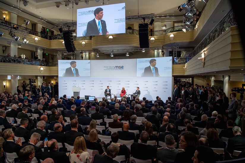 Defense Secretary Dr. Mark T. Esper sits on a stage with two people in front of a large audience.