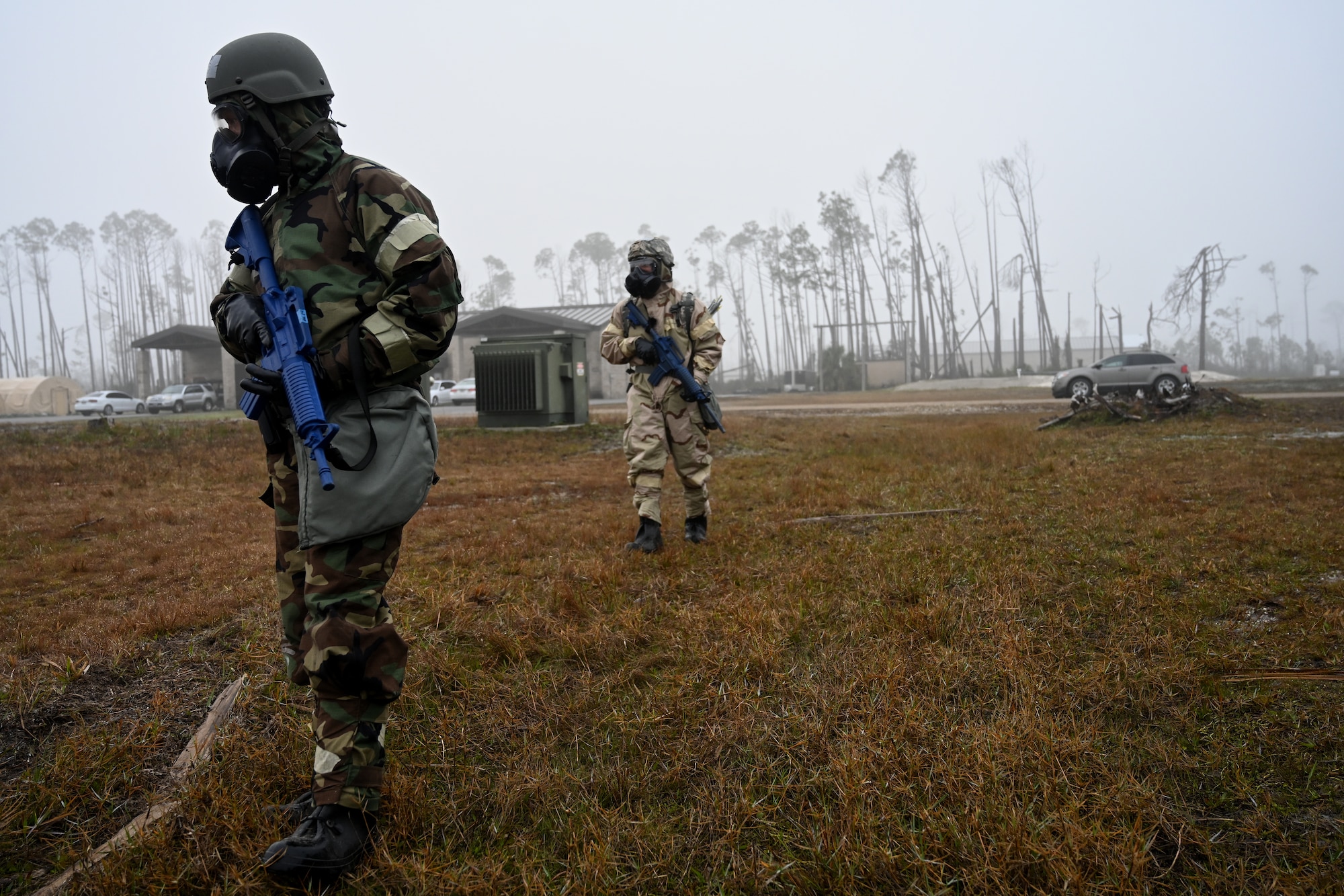 Airmen in chemical warfare gear patrolling with rifles.