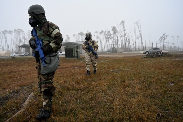 Airmen in chemical warfare gear patrolling with rifles.