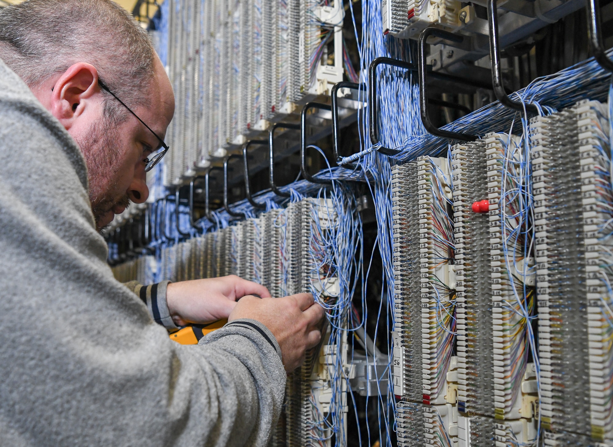 Adam Marshall, a telephone technician, connects a phone line, Dec. 12, 2019, using a punch-down block on the main distribution frame in the Telephone Switchroom at Arnold Air Force Base, Tenn. (U.S. Air Force photo by Jill Pickett)